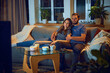 © master1305 - Loving young couple, man and woman sitting on sofa in evening at home,, hugging, cuddling and watching tv together. Concept of family, leisure time, relaxation, childhood and parenthood