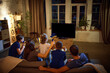 © master1305 - Back view. Family, parents and children sitting on couch in evening at home and watching football match translation. Concept of family, leisure time, relaxation, childhood and parenthood