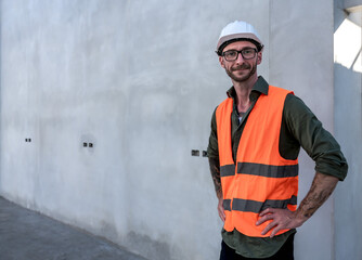 Caucasian construction worker man in safety uniform, vest and helmet standing in site, young home builder working at new house