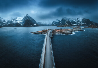 Wall Mural - aerial view of bridge, island with rorbu, sea, snowy mountains in fog, blue cloudy sky at twilight i