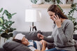 Sad sick preteen kid girl lying on sofa feel fever catch cold flu influenza. Anxious mom holding phone to ear make call to doc family therapist after measuring child temperature. Calling family doctor