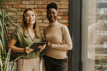 Wall Mural - Two young business women with digital tablet standing by the brick wall in the industrial style office