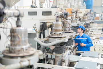 Wall Mural - Wide angle shot of American male engineer, technician manager Checking the orderliness of the machinery in the company's steel and plastic manufacturing plants. Wear a uniform and safety helmet.