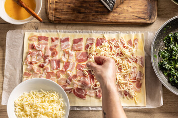 The female cook prepares mini pizza cakes, sprinkles cheese on puff pastry with bacon.