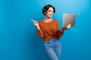 Wall Mural - Photo portrait of attractive young woman hold netbook point empty space dressed stylish brown clothes isolated on blue color background