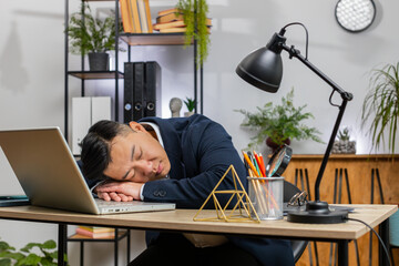 Wall Mural - Bored sleepy Asian businessman worker working on laptop computer, leaning on hand falling asleep at office desk. Exhausted tired freelancer workaholic Chinese middle-aged man. Employment, occupation