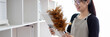 © Puwasit Inyavileart - Housewife holding a dusting brush to clean things Pillows, rugs and other things in the living room, Big cleaning, Daily routine, Clean up on weekends.