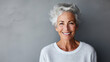 © Santy Hong - Close up portrait of beautiful older woman smiling and standing by grey wall.