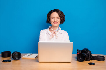 Sticker - Photo of charming lady sit behind desk use laptop smile look camera isolated on blue color background