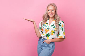 Poster - Portrait of toothy beaming woman with wavy hair wear stylish shirt arm presenting offer look empty space isolated on pink color background