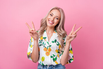 Poster - Portrait of positive cute woman with wavy hairstyle wear stylish print shirt two hands show v-sign isolated on pink color background