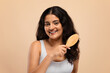 © Prostock-studio - Smiling beautiful indian woman brushing her thick curly hair with bamboo comb