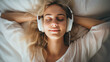 Young beautiful blond woman smile and listen music while lying on her bed. Happy girl fall asleep listening to relaxing music with headphones. Closeup face portrait. 