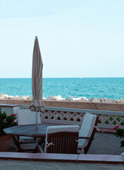 Wall Mural - Terrace with wooden table and chairs with parasol on a sunny Mediterranean beach