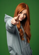 © Julia Zarubina - young red-haired girl in a purple hoodie points with her finger, teenager, student, color background, beautiful woman, fashion, style, portrait, hairstyle, face, pointing gesture