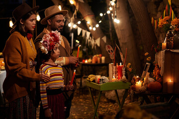 Wall Mural - Family of three standing in front of altar with candles and celebrating the mexican holiday