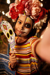 Wall Mural - Vertical portrait of little girl with skull mask looking at camera while celebrating traditional holiday