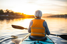 Rear view of a retired older woman enjoying a peaceful moment while canoeing or kayaking on calm waters during late afternoon. A serene scene, contemplative solitude and tranquility