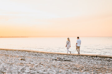 A charming couple in a white shirt walks along the shore at sunset in summer,rear view. Togliatti, Russia - 15 Aug 2023