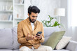 © Liubomir - Sad unhappy and disappointed man sitting at home on sofa in living room, Indian man received notification message with bad news, reading using smartphone app.