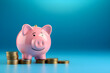 © Carlos Montes - Smiling pink pig piggy bank next to a stack of gold coins, isolated on blue background. Investment success, savings concept