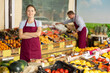 © JackF - Confident successful young saleswoman in maroon apron standing with arms crossed among colorful stands with ripe fresh organic fruits and vegetables in greengrocery, looking at camera with smile