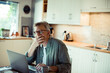 © Davor - Mature middle aged senior man holding hand over mouth using laptop at home