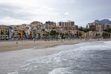 Canvas Print - Sea waves splashing over the shore with the city in the background, Alicante, Spain