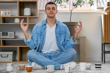 Sticker - Handsome young man with many cups of coffee meditating on floor in living room