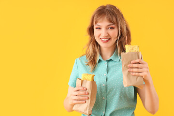 Poster - Young woman with tasty sandwich wraps on yellow background