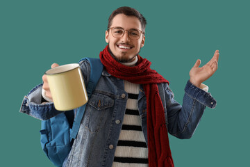 Poster - Young man in winter clothes with cup of hot tea on green background