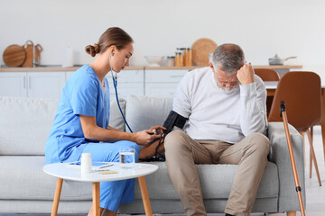 Canvas Print - Nurse measuring blood pressure of senior man at home