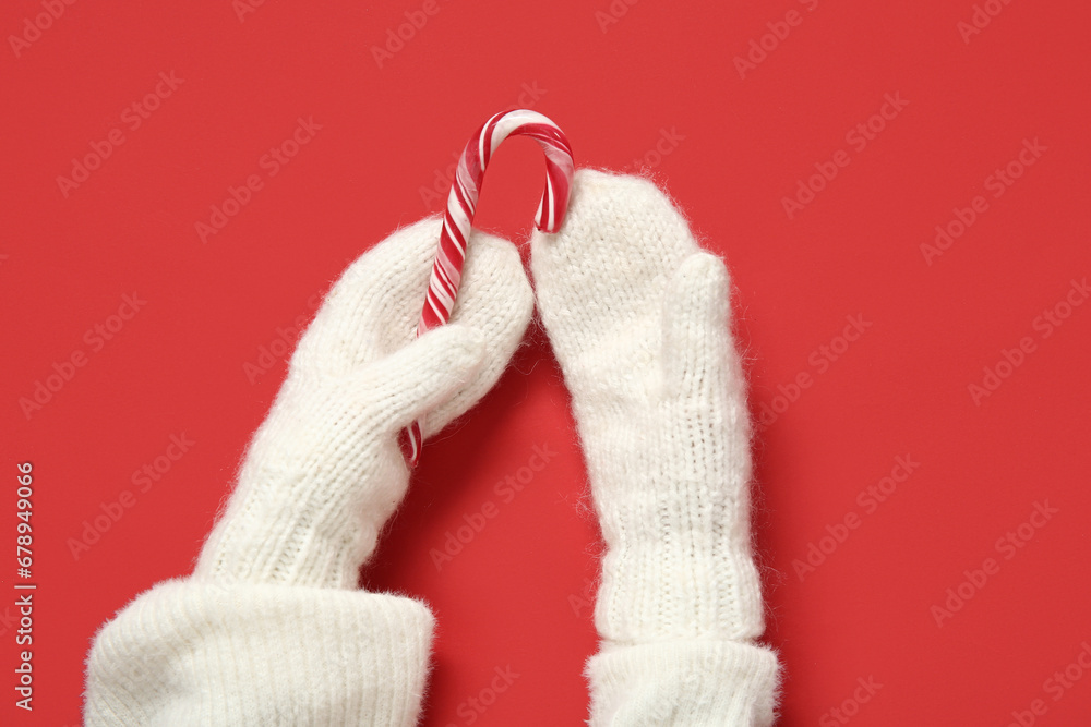 Female hands in knitted warm mittens with candy cane on red background, closeup