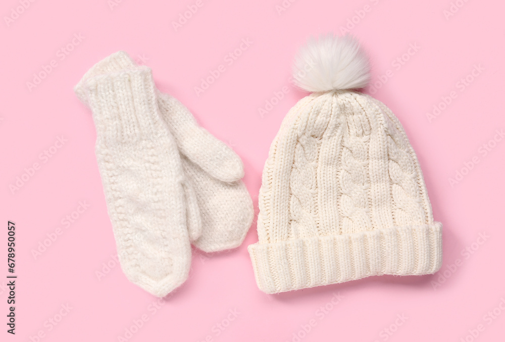 Pair of white knitted mittens with warm hat on pink background