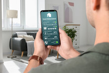 Man using smart home control system via application on mobile phone indoors, closeup