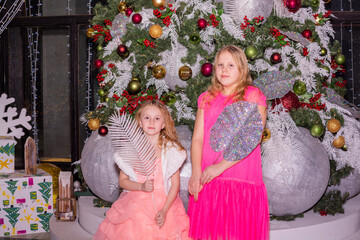 Wall Mural - Beautiful elegant girls near the Christmas tree in the New Year. Holiday. New Year. Children are models. Two sisters.