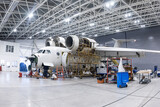 Fototapeta  - White transport aircraft in the aviation hangar. Airplane under maintenance. Checking mechanical systems for flight operations