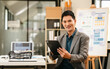© Phushutter - Attractive professional Asian businessman with tablet in office environment, confidently smiling, possibly analyzing data as Capital Market Analyst.