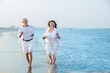 Happy senior indian couple wearing white cloths running together at beach and having fun. Vacations and Health Concept