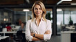 © Athena - A confident and stylish white businesswoman, surrounded by the sleek furnishings of her office, stands with arms crossed and a warm smile, embodying diversity and strength in her work
