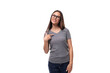 well-groomed young woman in glasses dressed in a gray t-shirt points to the space for advertising