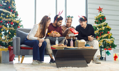 Millennial Asian Indian multinational cheerful male female friends celebrate Christmas Eve and Happy New Year holding showing presents gifts boxes in living room full decoration with Xmas tree