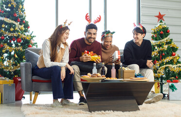 Millennial Asian Indian multinational cheerful male female friends celebrate Christmas Eve and Happy New Year holding showing presents gifts boxes in living room full decoration with Xmas tree