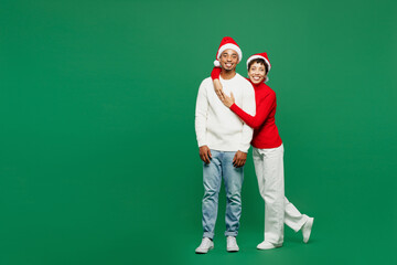 Wall Mural - Full body cheerful lovely merry young couple man woman wear red casual clothes Santa hat posing hugging embrace cuddle isolated on plain green background Happy New Year 2024 Christmas holiday concept