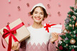 Merry young woman wear white sweater hat posing hold present box gift certificate coupon voucher card for store isolated on plain pink background. Happy New Year celebration Christmas holiday concept.