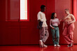 © Seventyfour - Diverse group of gen Z young people standing against red metal wall in futuristic office space