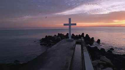 Wall Mural - A flight around a Christian Holy cross early in the morning at sunrise. The large cross stands on the edge of a breakwater on the sea coast