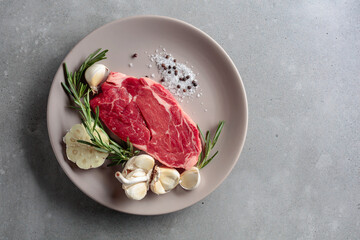 Fototapeta raw beef steak with rosemary, garlic, salt, and pepper.