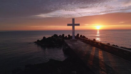 Wall Mural - A flight around a Christian Holy cross early in the morning at sunrise. The large cross stands on the edge of a breakwater on the sea coast