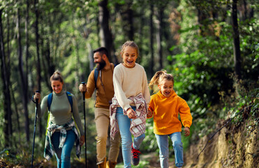 Wall Mural - Smiling family of four enjoying hiking in trough forest.